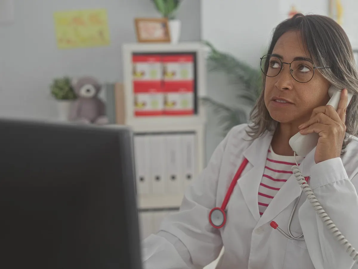 Stock photograph of a model: a doctor in a white coat talks on a desk telephone in her office