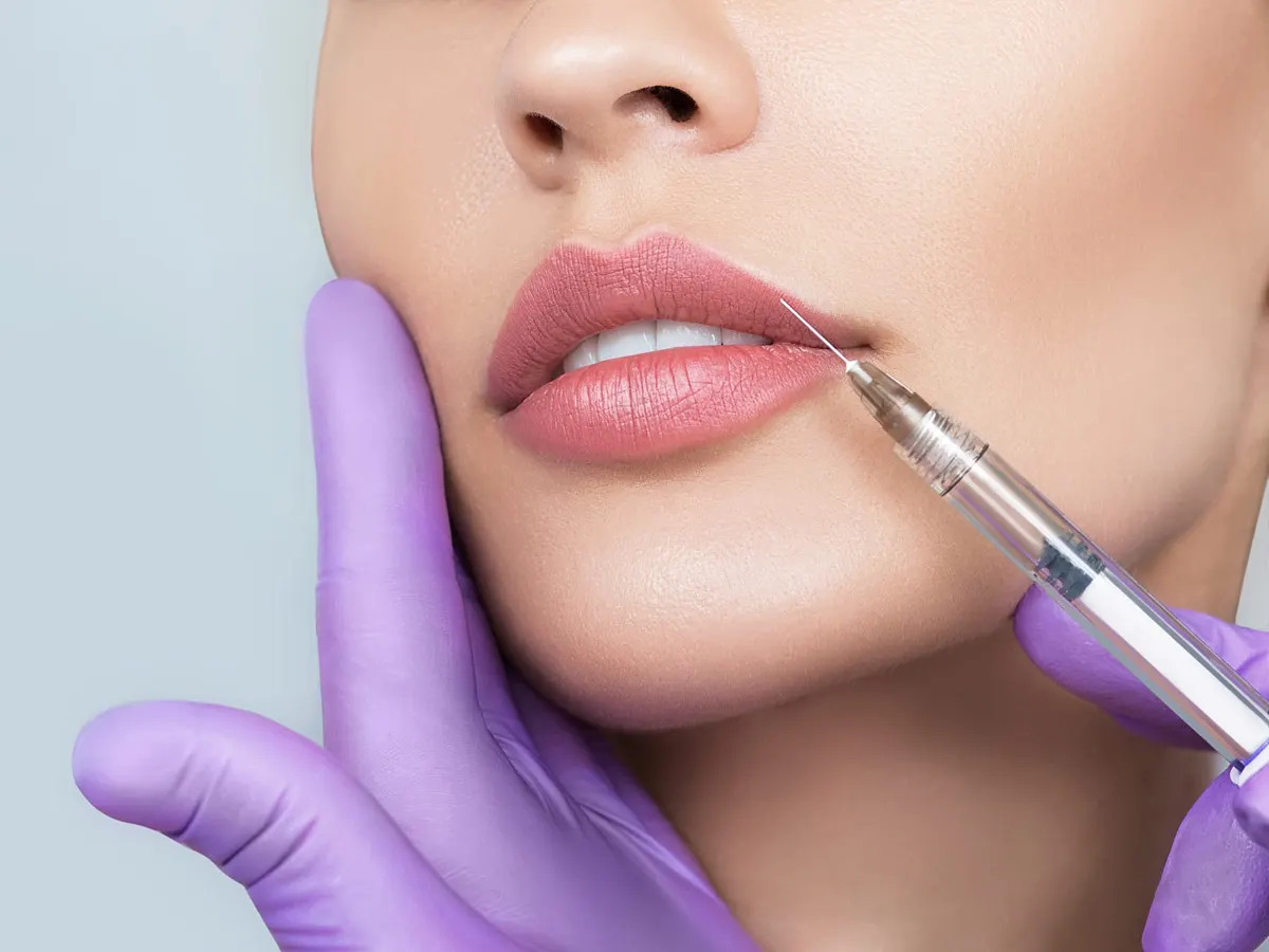 Stock photograph of a model: a purple-gloved hand steadies a woman's chin as a fine needle touches her upper lip