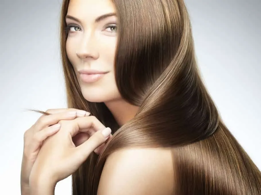 A model with long, glossy brown hair looking over her shoulder, fingers touching a strand