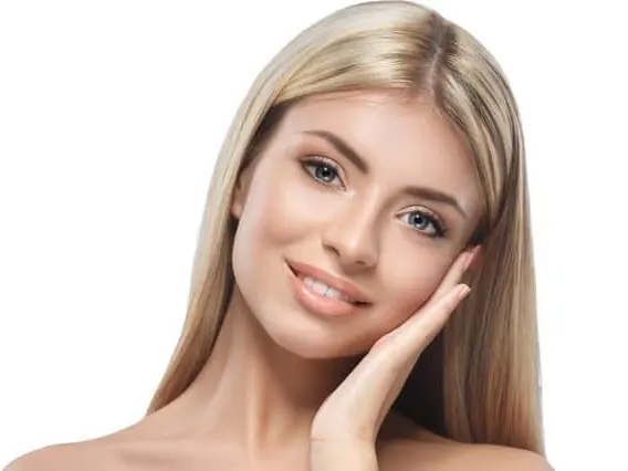 A model with long blonde hair smiling with a hand against her cheek