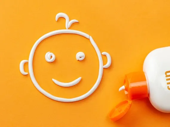 Plastic bottle of sun protection and white cream in the shape of a smiling baby face