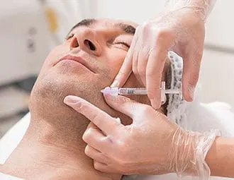 A gloved hand injecting filler along a man's jawline while he lies back with eyes closed