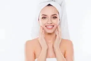 A model with a towel wrapped on her head smiling, hands touching her cheeks