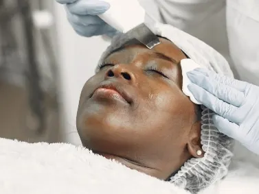 A woman lying back with eyes closed while a gloved hand performs a facial treatment