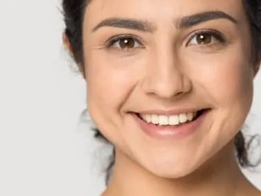 A smiling model with dark hair and clear skin looking at the camera