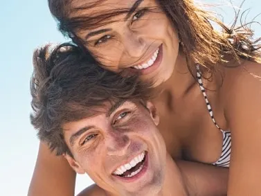 Models, a smiling man giving a woman a piggyback at the beach under blue sky
