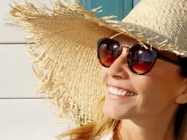 A smiling model in a straw sun hat and sunglasses outdoors