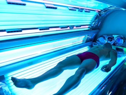 A man lying on a tanning bed under blue lights