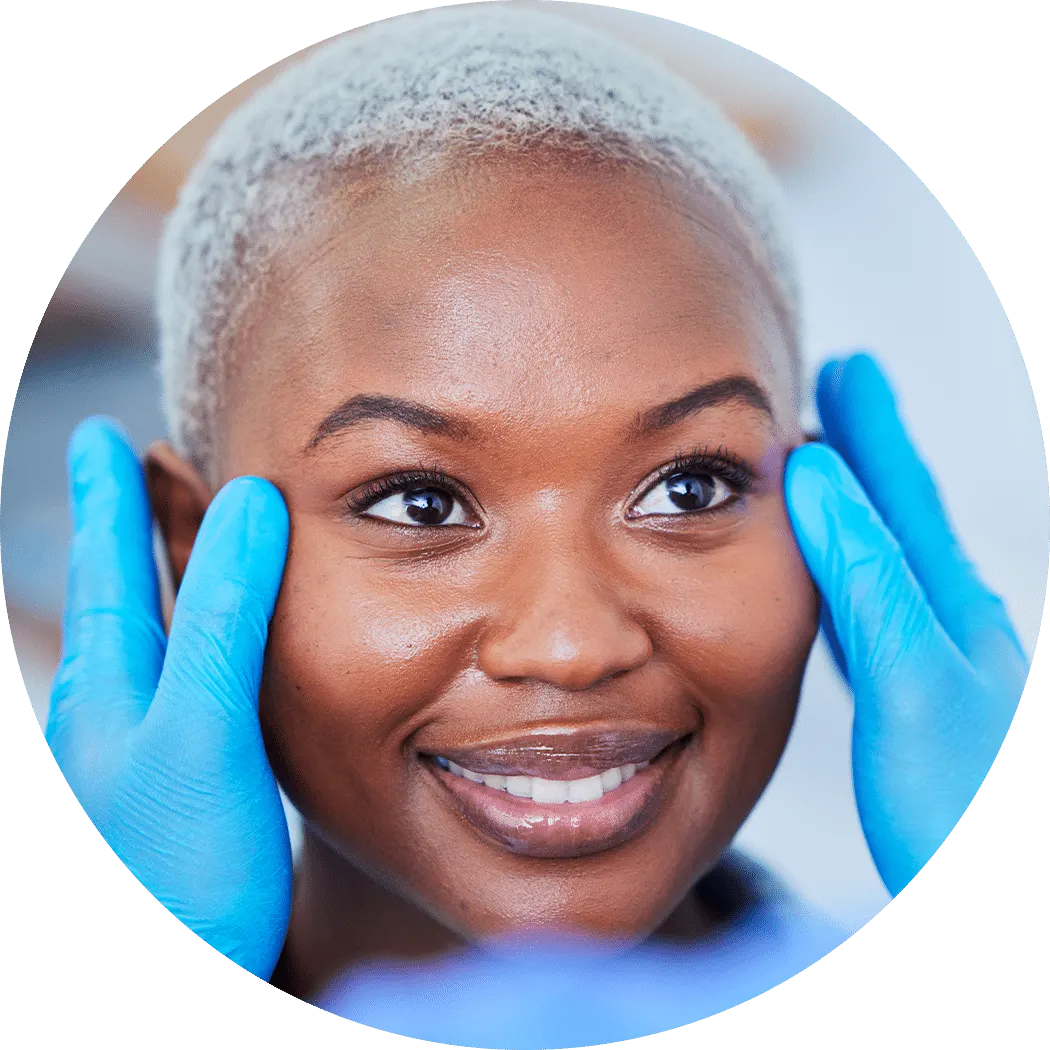 A smiling woman with short grey-blonde hair as blue-gloved hands frame her eyes