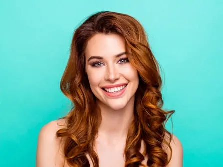 Beautiful woman standing in front of teal wall has smooth skin after treating acne scars.