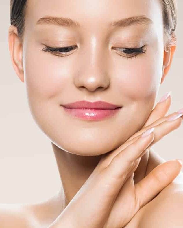 Stock photograph of a model: a young woman with smooth, glowing skin smiles with her eyes closed and a hand at her jaw