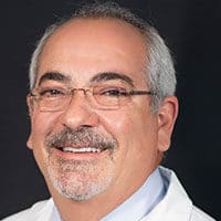 Dr. Martin N. Zaiac, smiling, with grey hair and glasses, in a white coat