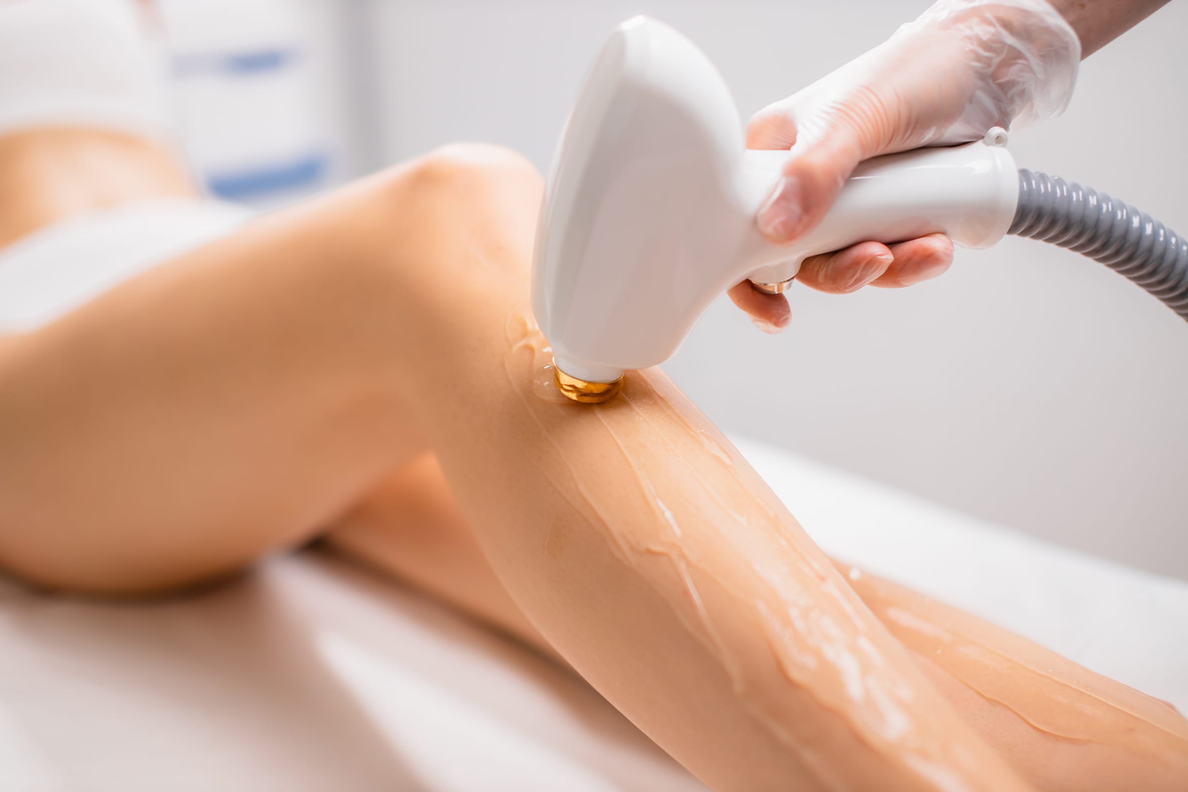 Stock photograph of a model: a laser hair removal handpiece glides along a woman's lower leg
