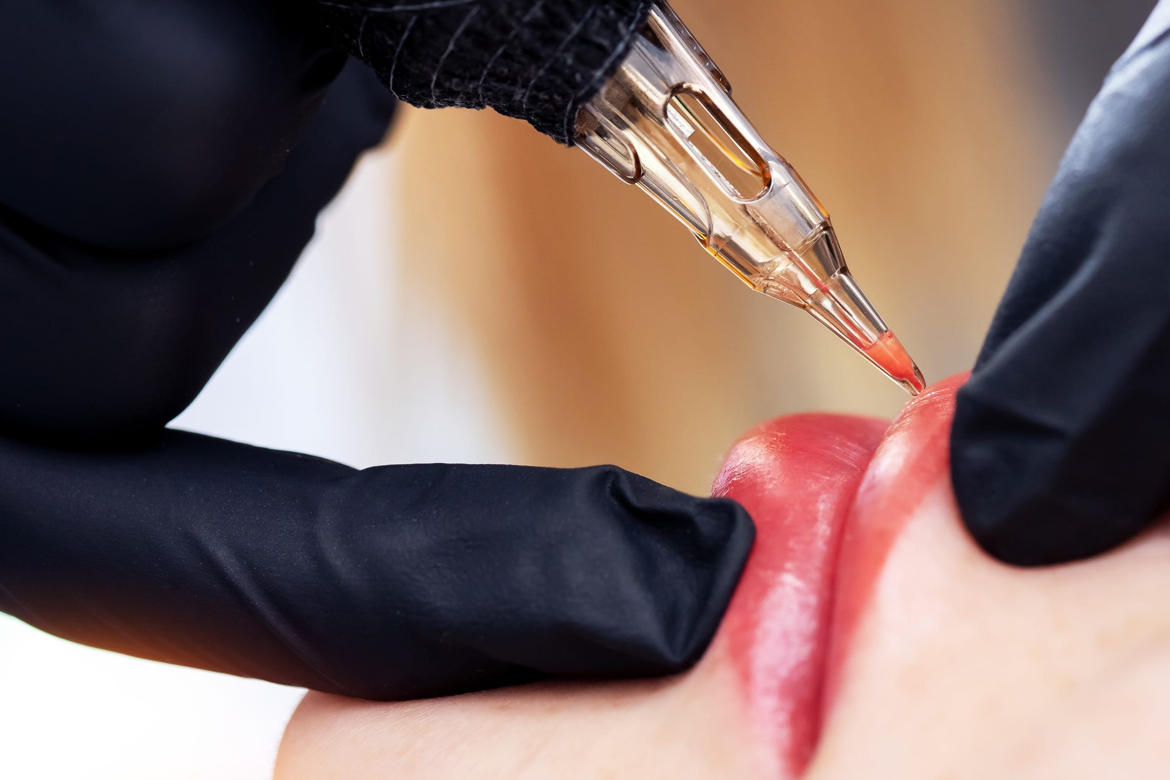 Stock photograph of a model: black-gloved hands apply red pigment to a woman's lip line with a fine tattoo needle