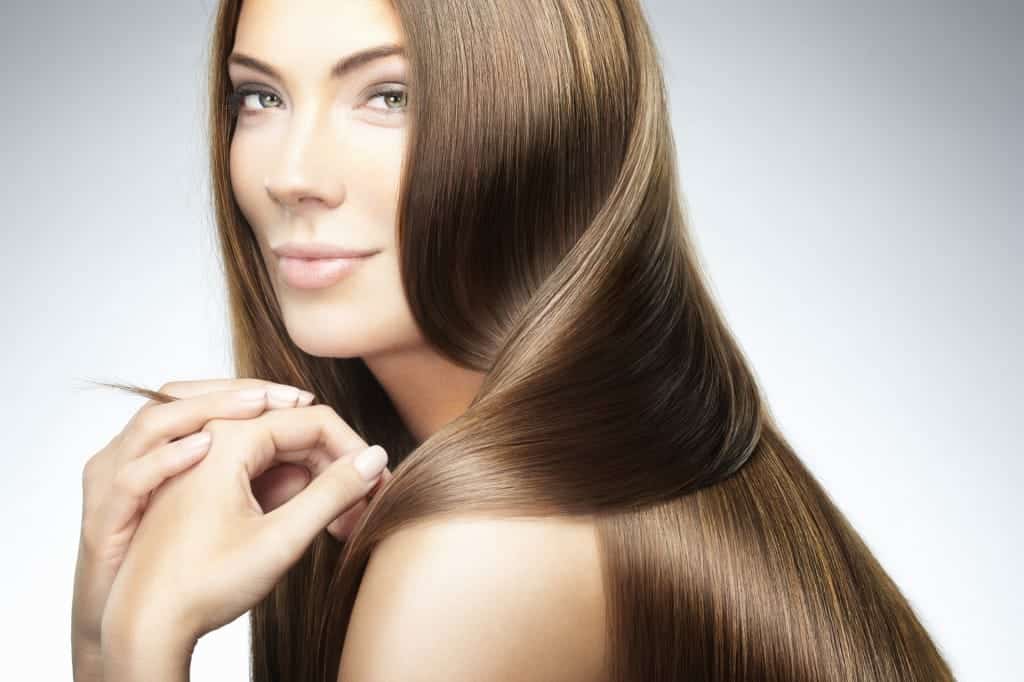 A model with long, glossy brown hair looking over her shoulder, fingers touching a strand