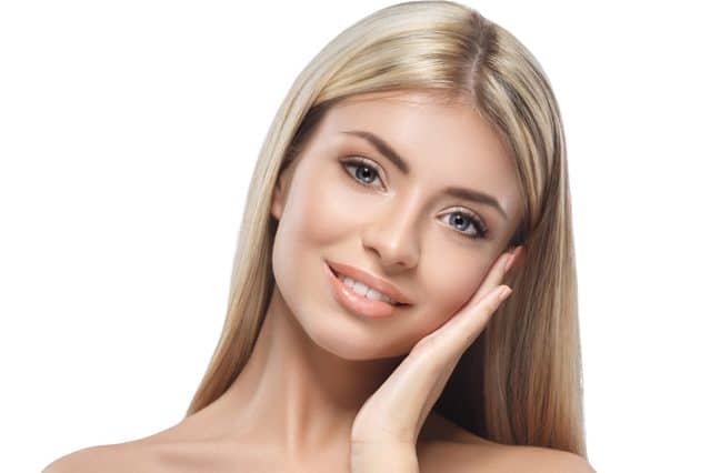 A model with long blonde hair smiling with a hand against her cheek