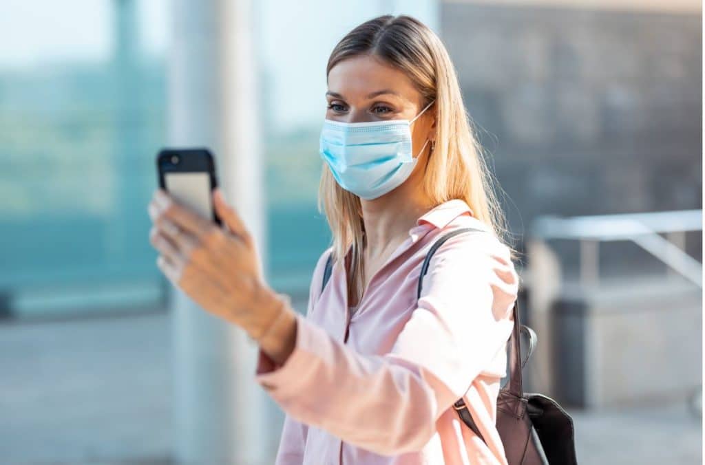 A model wearing a face mask taking a selfie with her phone outdoors