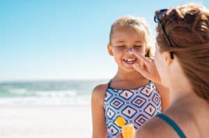 Two models, a mother and a young girl, as she applies sunscreen to the girl's nose at the beach