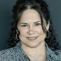 Onelia Valdes, Office Manager, smiling, with dark curly hair and hoop earrings