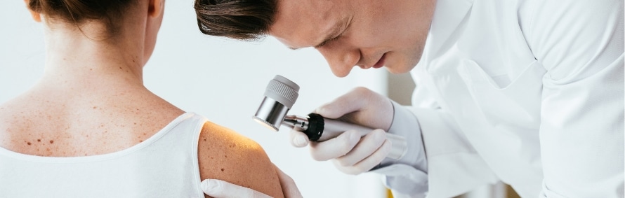 A dermatologist examining a woman's back and shoulder with a handheld dermatoscope