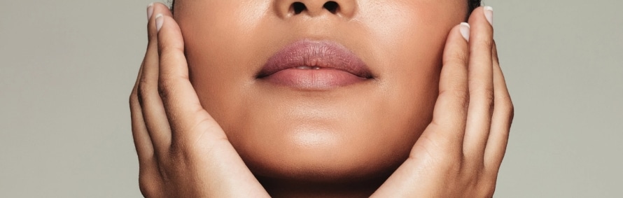 A model cradling her jaw in both hands, showing smooth skin around the lips and chin