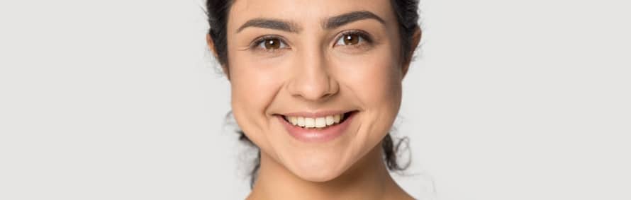 A smiling model with dark hair and clear skin looking at the camera