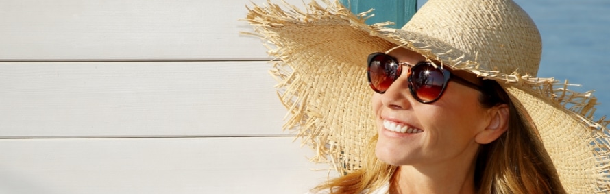 A smiling model in a straw sun hat and sunglasses outdoors