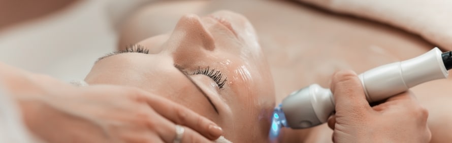 A model lying back with eyes closed during a facial treatment with a handheld device