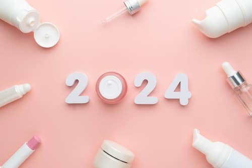 Skincare bottles, jars and droppers on a pink background around the number 2024