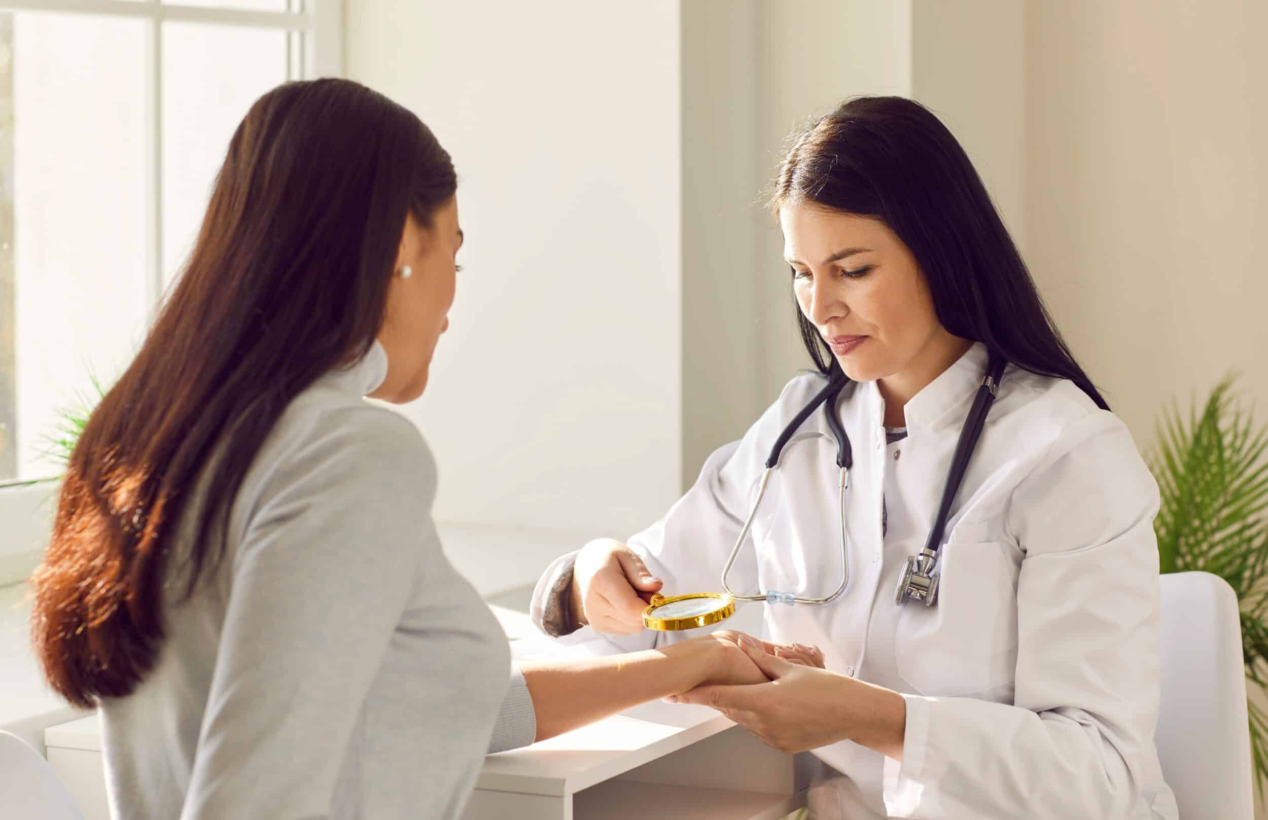 A dermatologist in a white coat examining a model's hand with a magnifying glass