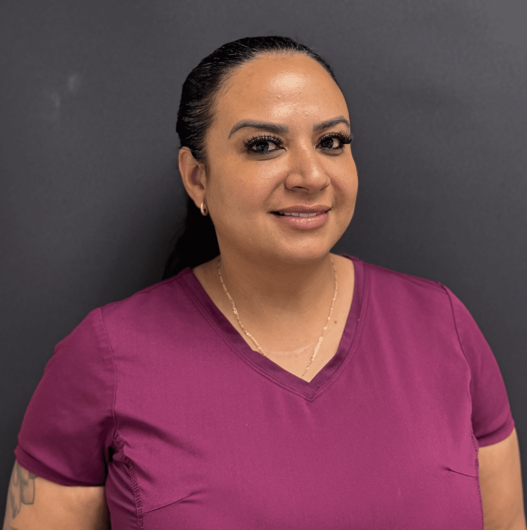 Jurany Baena, Check In Coordinator, smiling, with dark hair pulled back, in plum scrubs