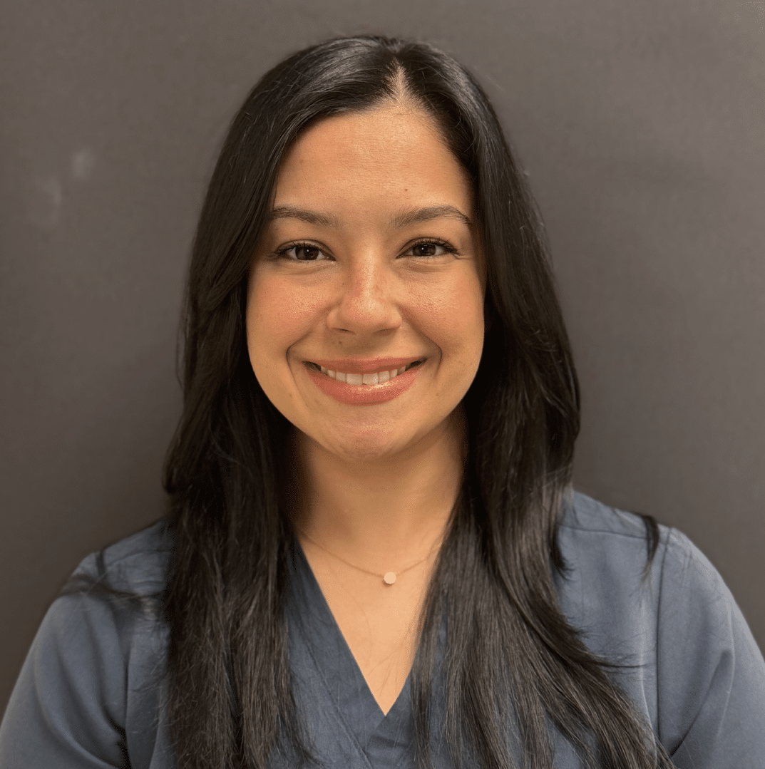 Melanie Santos, Medical Assistant, smiling, with long dark hair, in grey scrubs