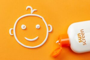 Plastic bottle of sun protection and white cream in the shape of a smiling baby face