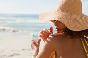 woman on the beach putting sunscreen on her shoulder