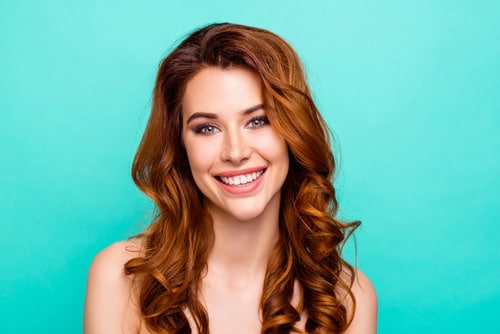 Beautiful woman standing in front of teal wall has smooth skin after treating acne scars.